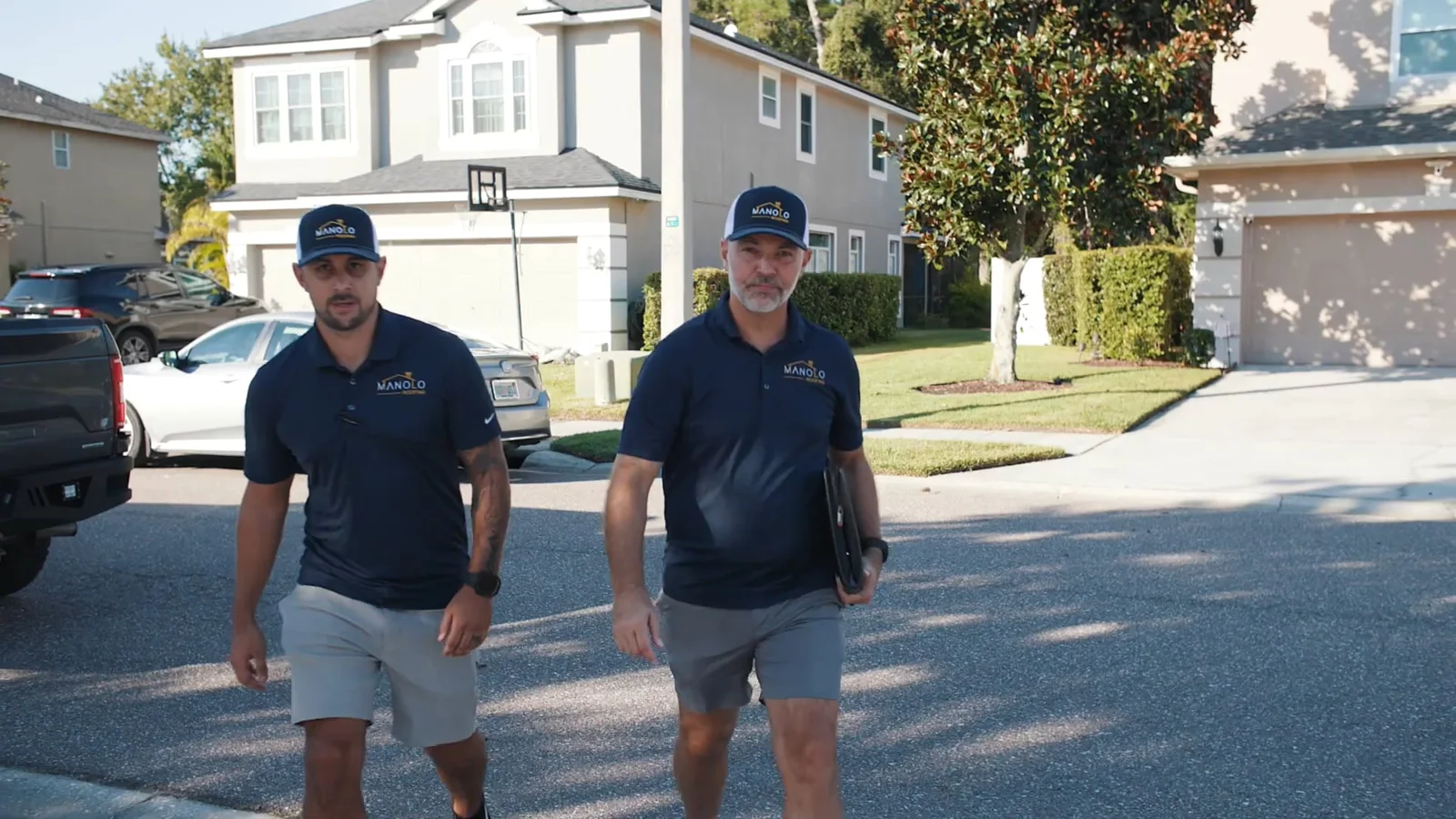 Two Manolo Roofing team members walking toward a home