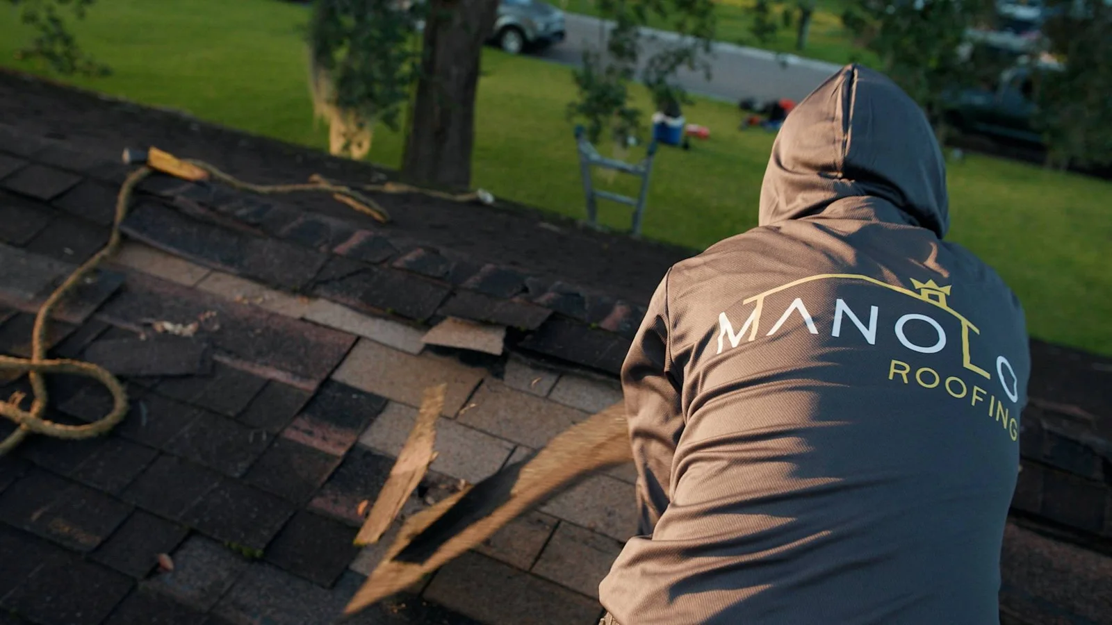 Crew member in a Manolo Roofing shirt removing old shingles