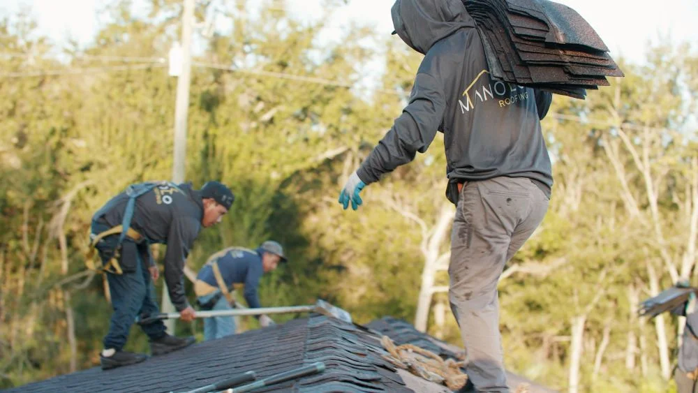 Manolo Roofing crew working on a roof with shingle bundles